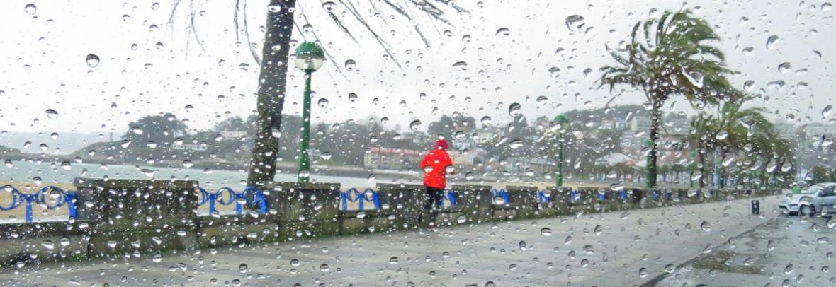 Main in red raincoat jogging in rain near beach